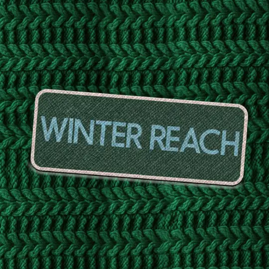 Dark green fabric patch with the words “Winter Reach” in bold teal capital letters, placed on a chunky dark green knit background.