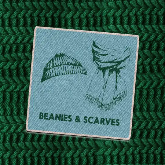 Teal fabric patch with a dark green illustration of a beanie and scarf with the words “Beanies & Scarves” in bold capital letters, placed on a chunky dark green knit background.