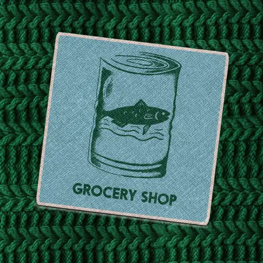 Teal fabric patch with a dark green illustration of canned tuna and the words “Grocery Shop” in bold capital letters, placed on a chunky dark green knit background.